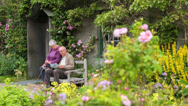 Two visitors sitting on a bench surrounded by pink flowers at Hill Top